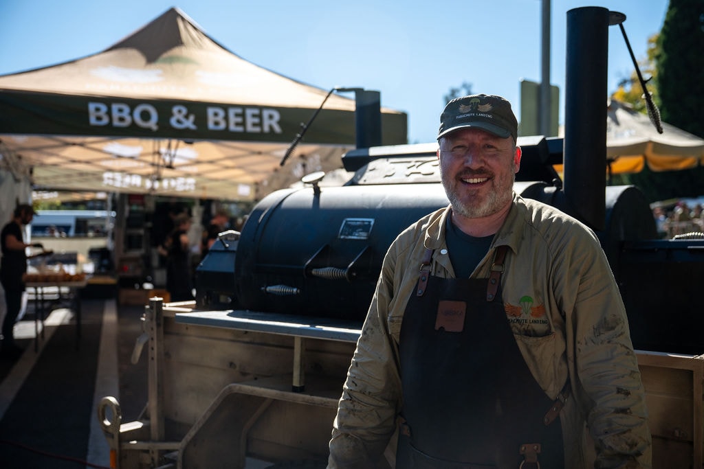 Mark, founder of Parachute Landing, smiling in front of the BBQ smoker at a BBQ & Beer event